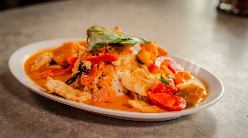 Red curry with chicken, bell peppers, and basil, served over white rice on a white plate.