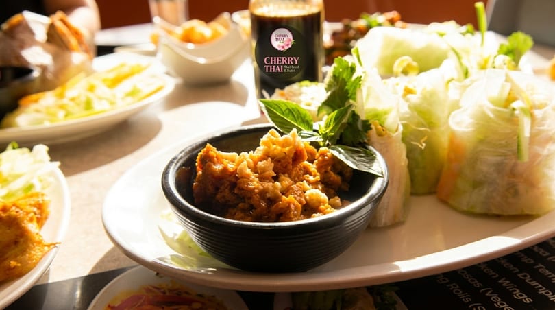 A close-up of Cherry Thai's lettuce wraps and a bowl of minced chicken, with other dishes blurred in the background.