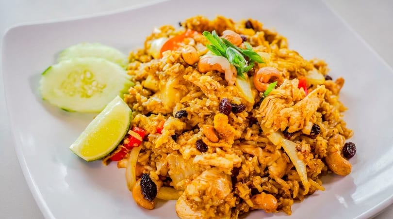 Close-up of pineapple fried rice with chicken, cashews, raisins, and vegetables, garnished with lime and cucumber.