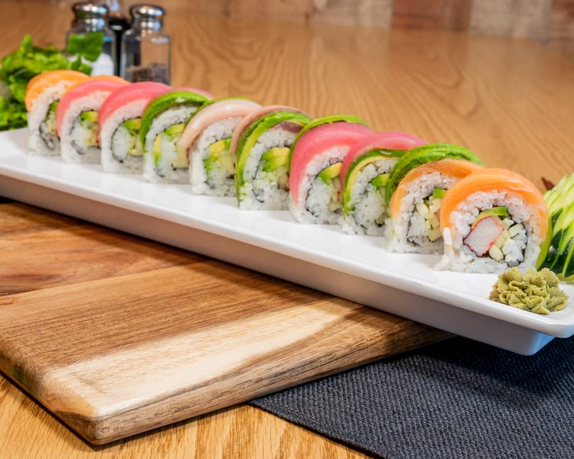 Colorful sushi rolls with salmon, tuna, and avocado on a white plate with wasabi.
