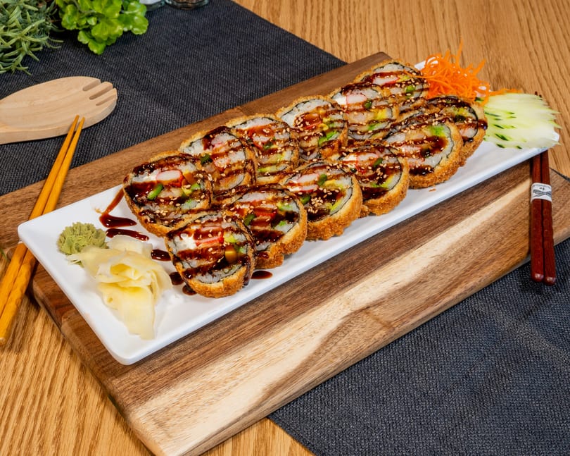 Crispy deep-fried sushi rolls with sauce, sesame seeds, ginger, and wasabi on a white plate.