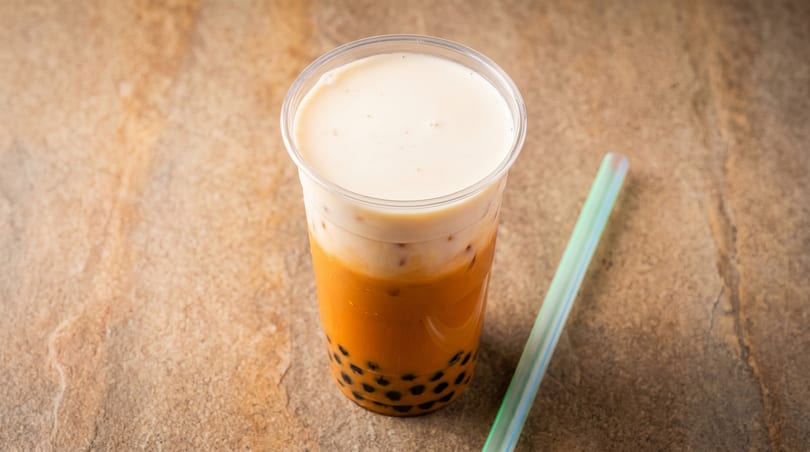 Thai milk tea with tapioca pearls and a creamy foam topping, next to a green straw.