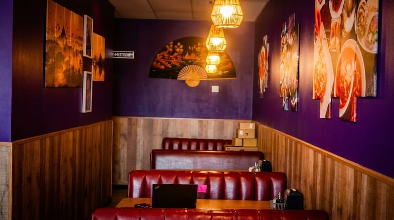 Restaurant interior with purple walls, wood paneling, red booths, and Asian-themed decor.