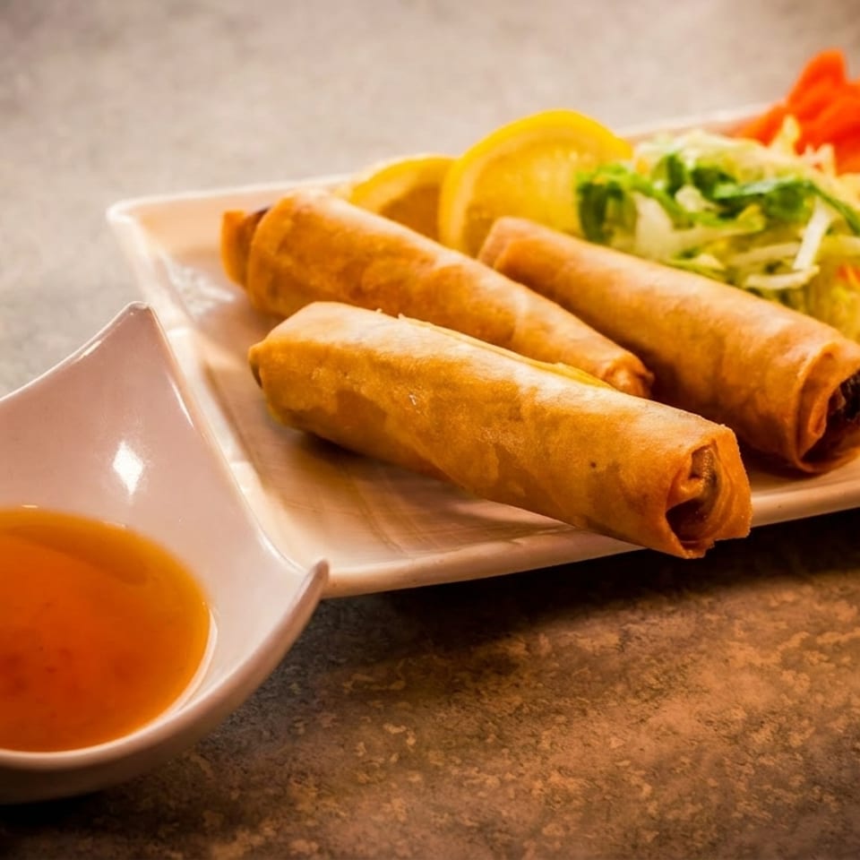 Crispy spring rolls with shredded lettuce, lemon, and a side of dipping sauce.