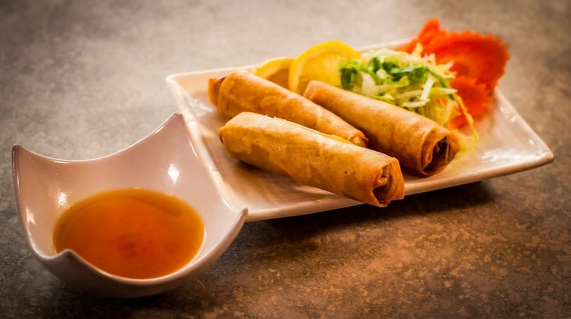 Crispy spring rolls with shredded lettuce, lemon, and a side of dipping sauce.