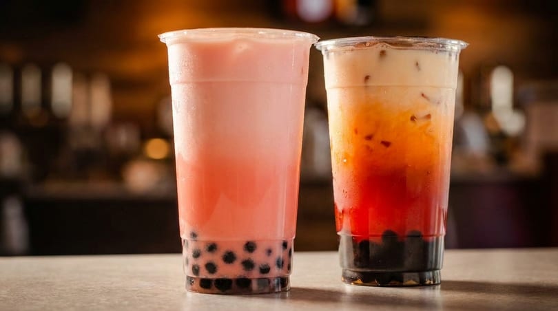 Two plastic cups of bubble tea, one pink and one orange and red, with tapioca pearls.
